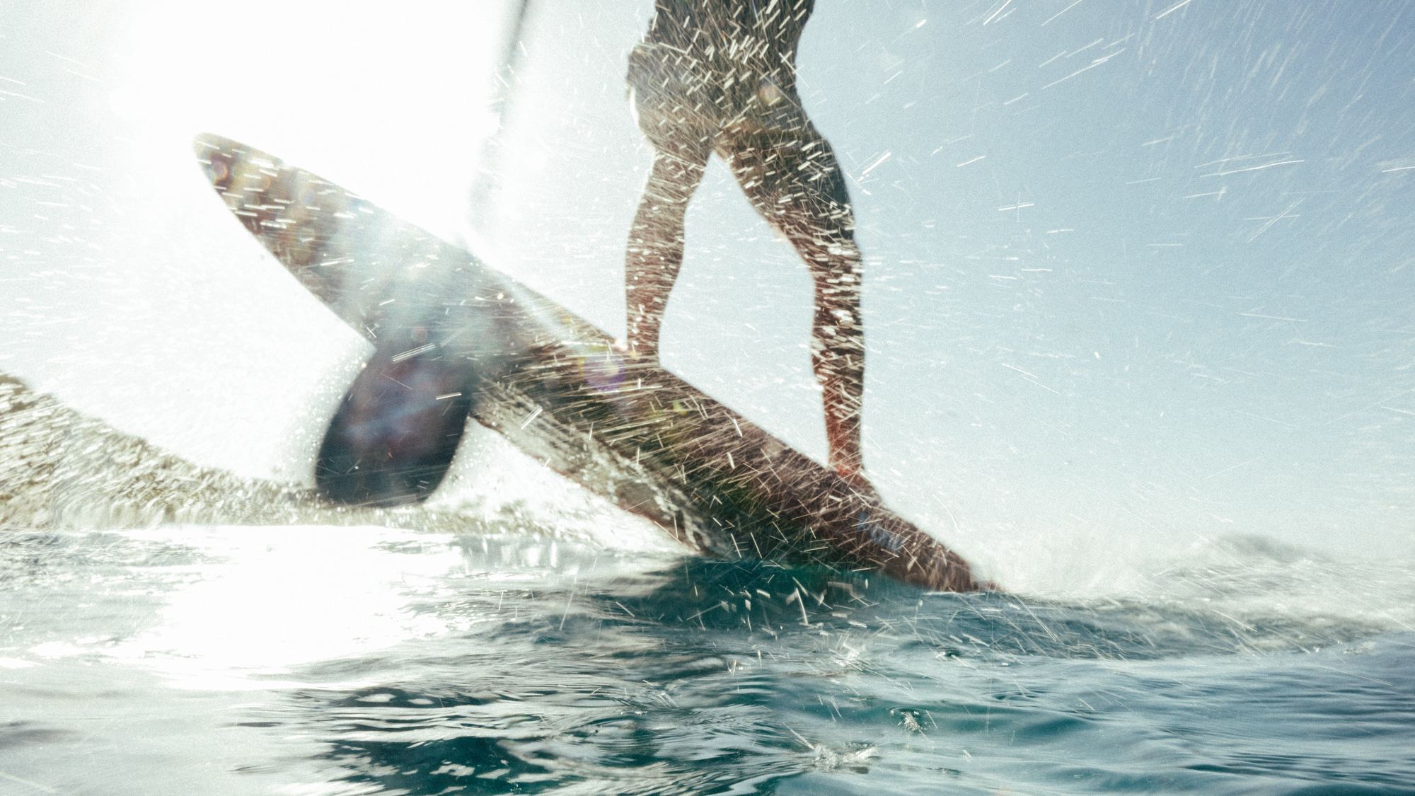 Surfer carving through spray in bright backlight
