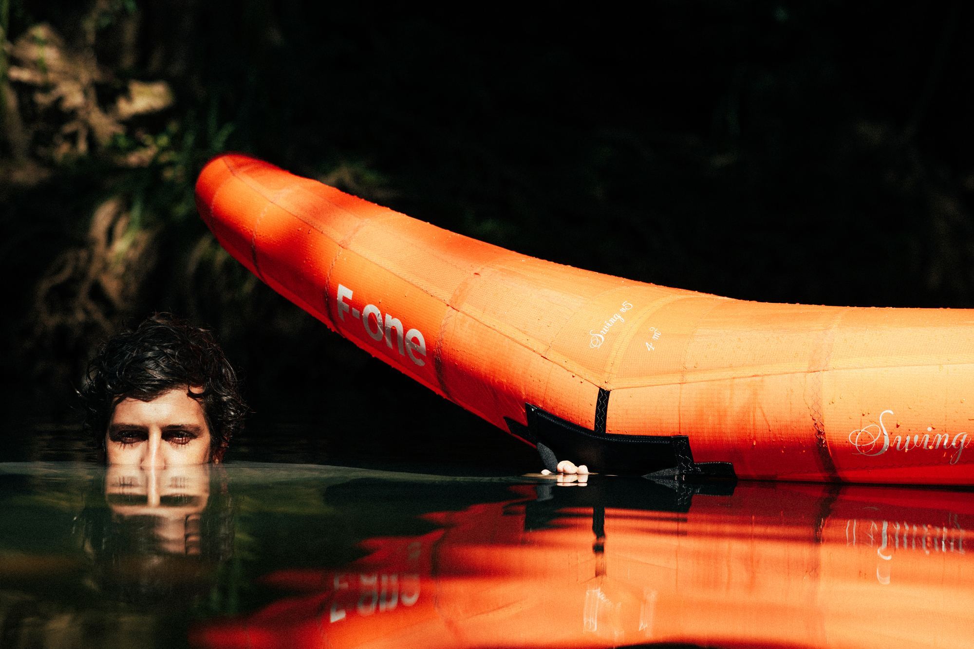 Person half submerged holding F-ONE kite in river